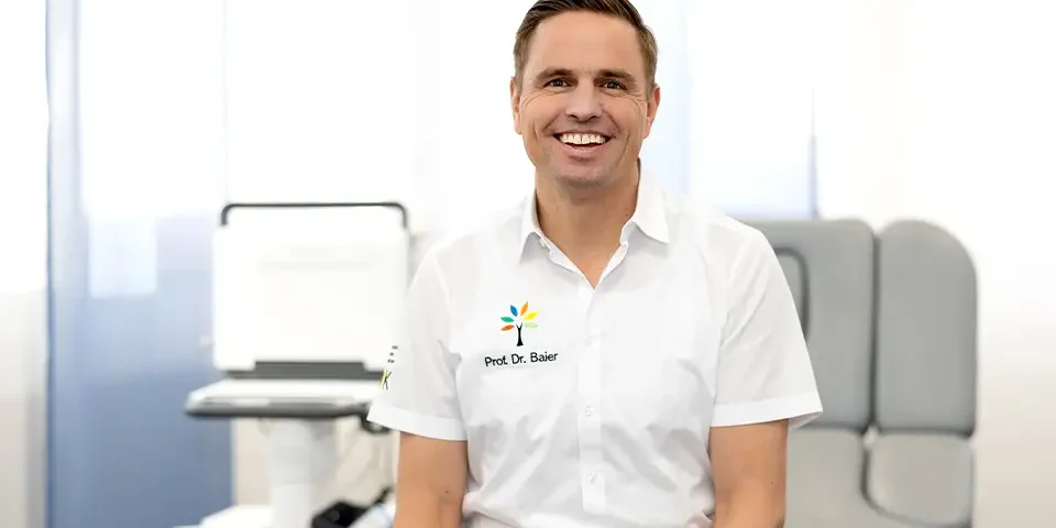 Porträt von lächelnden Prof. Dr. Clemens-Baier,– Facharzt für Orthopädie, welcher in einem Behandlungsraum sitzt