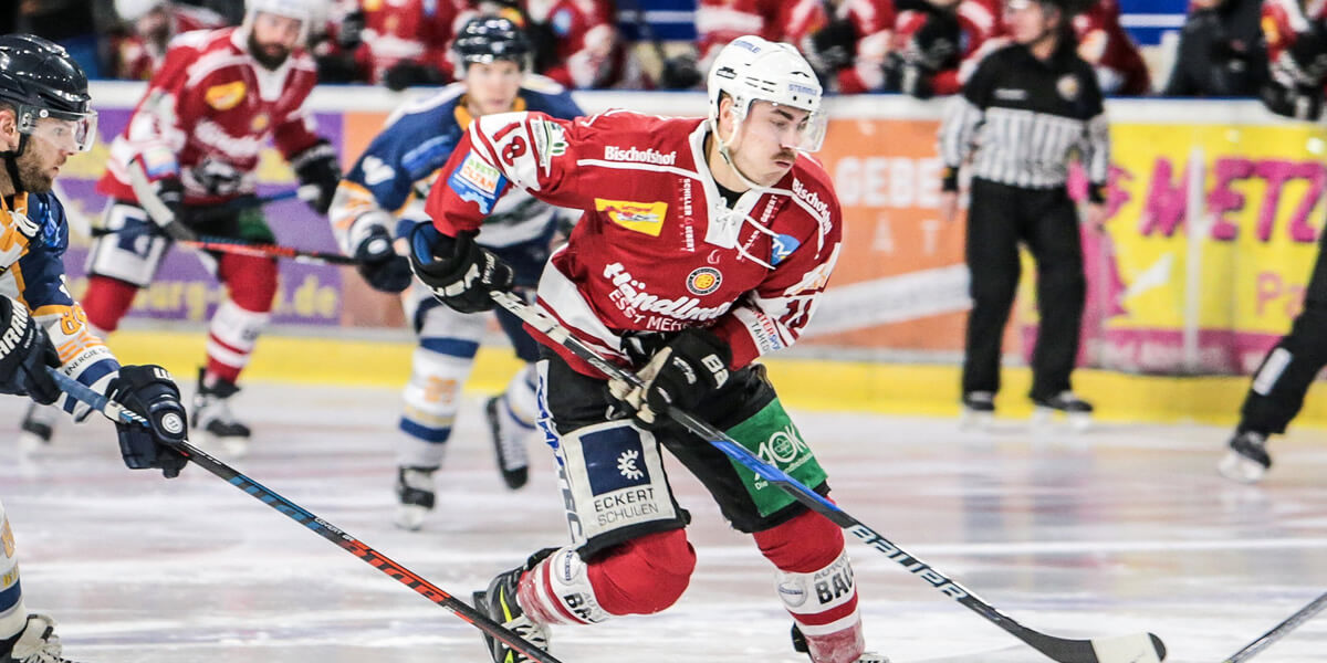 Eishockeyspieler Eishockeyspieler in Aktion auf dem Eis, zwei Spieler in rot-weißer und zwei in blau-weißer Ausrüstung kämpfen um den Puck, im Hintergrund Schiedsrichter und Zuschauer.